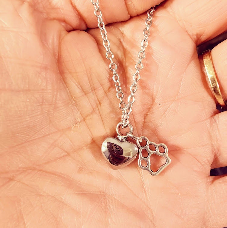 Silberne Herz-Urne mit Pfoten-Charm an Silberkette in einer Handfläche gehalten, Nahaufnahme – Gedenkschmuck von Zinou Minimanufaktur