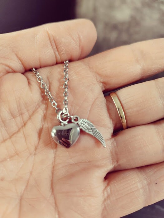 Silberne Miniurne Herz mit Flügel-Charm an Silberkette in einer Handfläche gehalten, Nahaufnahme – Gedenkschmuck von Zinou Minimanufaktur