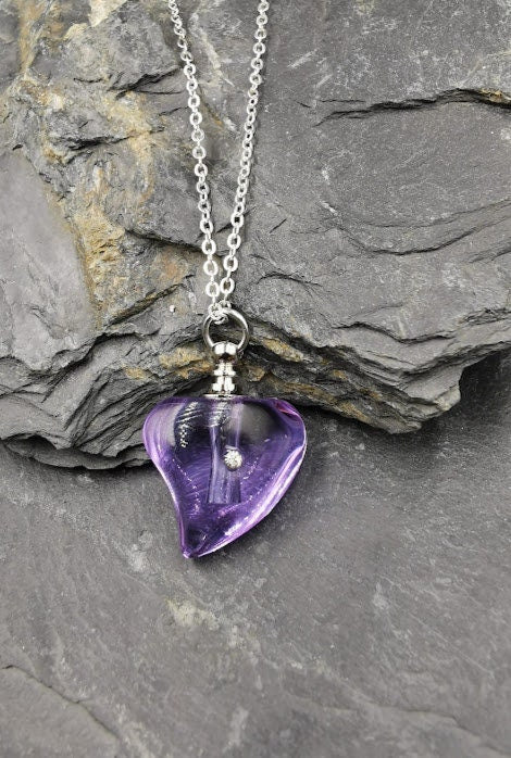 Violetter Glas-Herz-Urnenanhänger mit Strassstein an Silberkette auf Schieferstein vor dunklem Hintergrund – Miniurne Gedenkschmuck von Zinou Minimanufaktur
