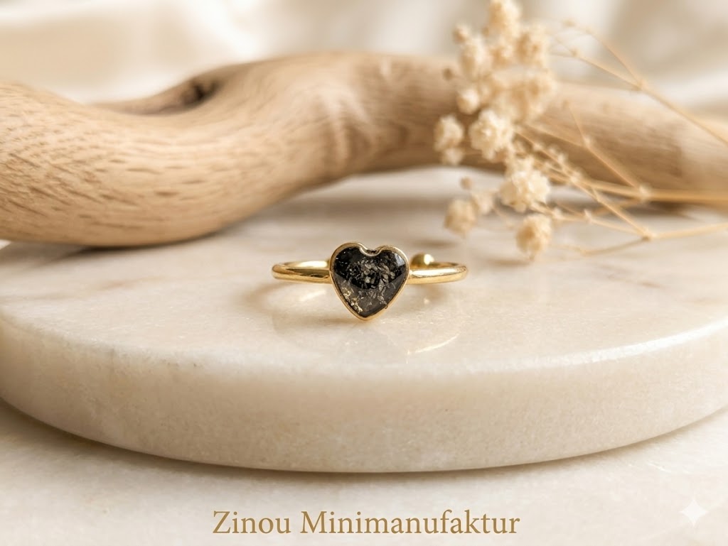 Goldener Herzring mit schwarzem Asche-Einschluss auf Marmorscheibe mit Treibholz und Trockenblumen – Gedenkring von Zinou Minimanufaktur
