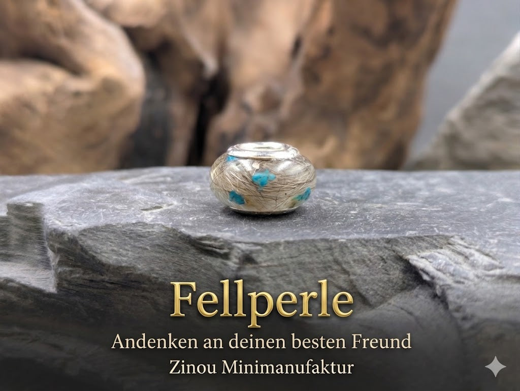 Eine runde Großlochperle mit Silberkern liegt auf einem dunklen Naturstein vor Holz-Hintergrund. Im Inneren der Perle sind feine Tierhaare und kleine leuchtend türkisblaue Blüten eingearbeitet. Auf dem Bild stehen die Schriftzüge „Fellperle“, „Andenken an deinen besten Freund“ und „Zinou Minimanufaktur“.
