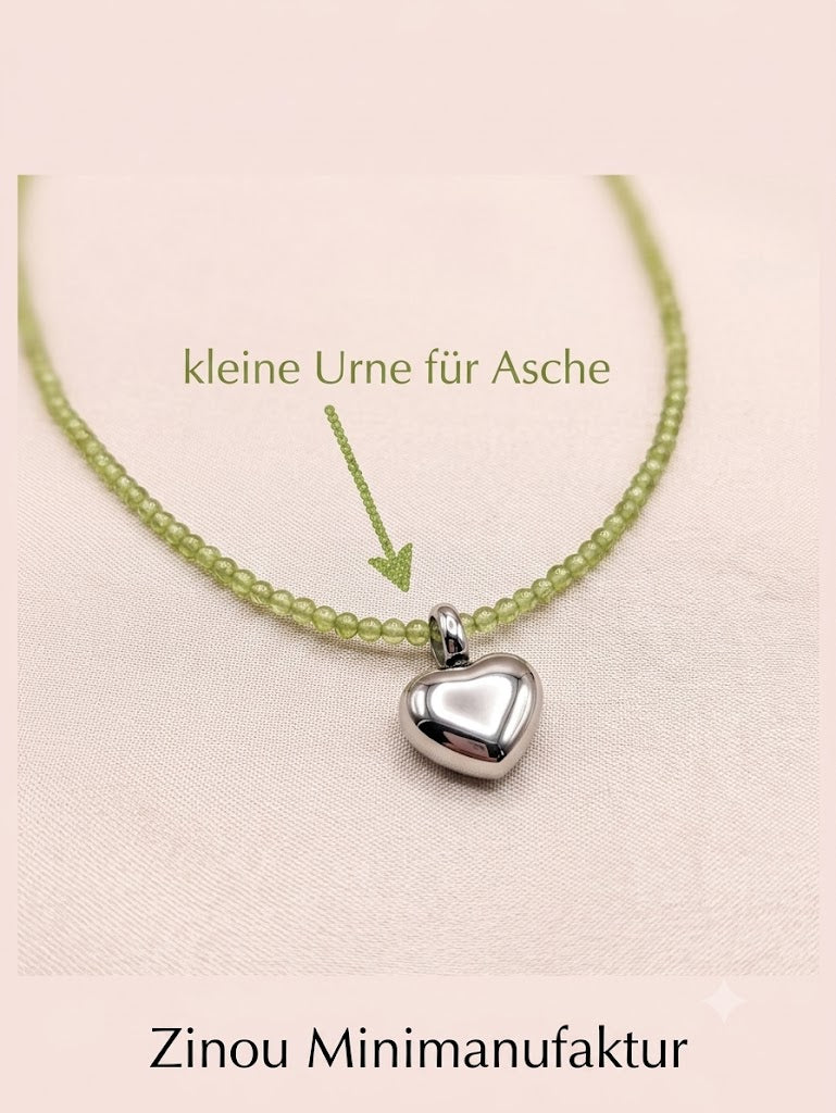silberne Herzurne aus Edelstahl auf olivgrüner Perlenkette unten steht Zinou Minimanufaktur kleine Urne zum befüllen von Asche