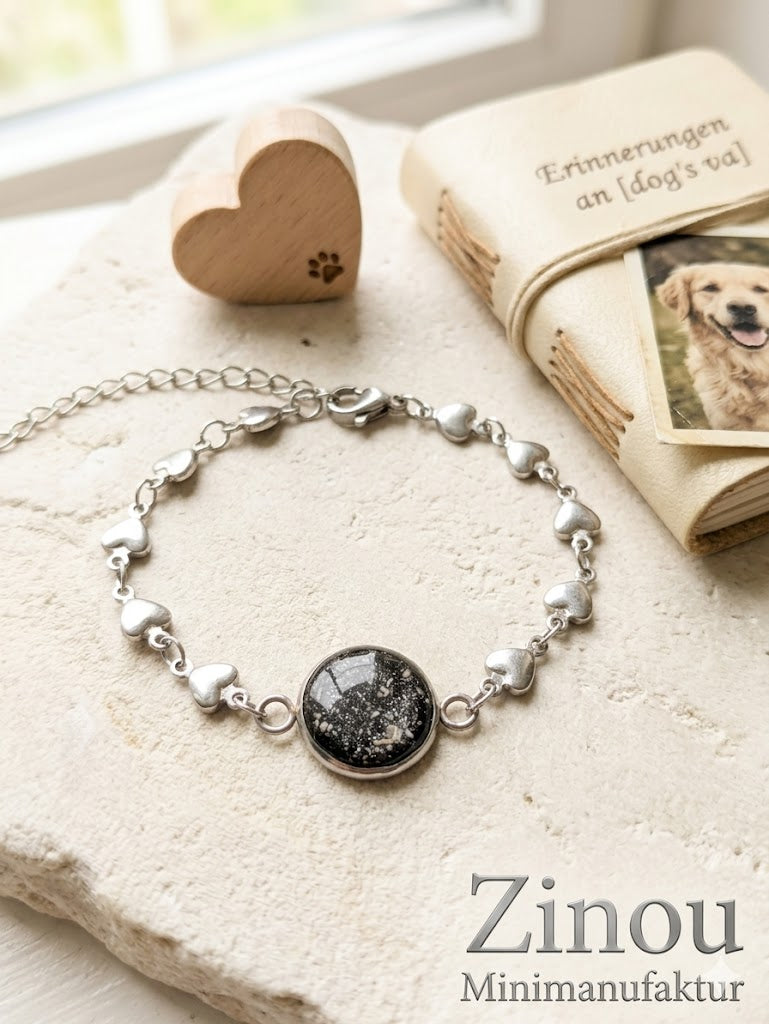 Silbernes Armband aus Edelstahl gefüllt mit Asche Untergrund ist schwarz versiegelt mit Harz. Ein Buch mit einem Foto von einem Labrador als Cover liegt dahinter 