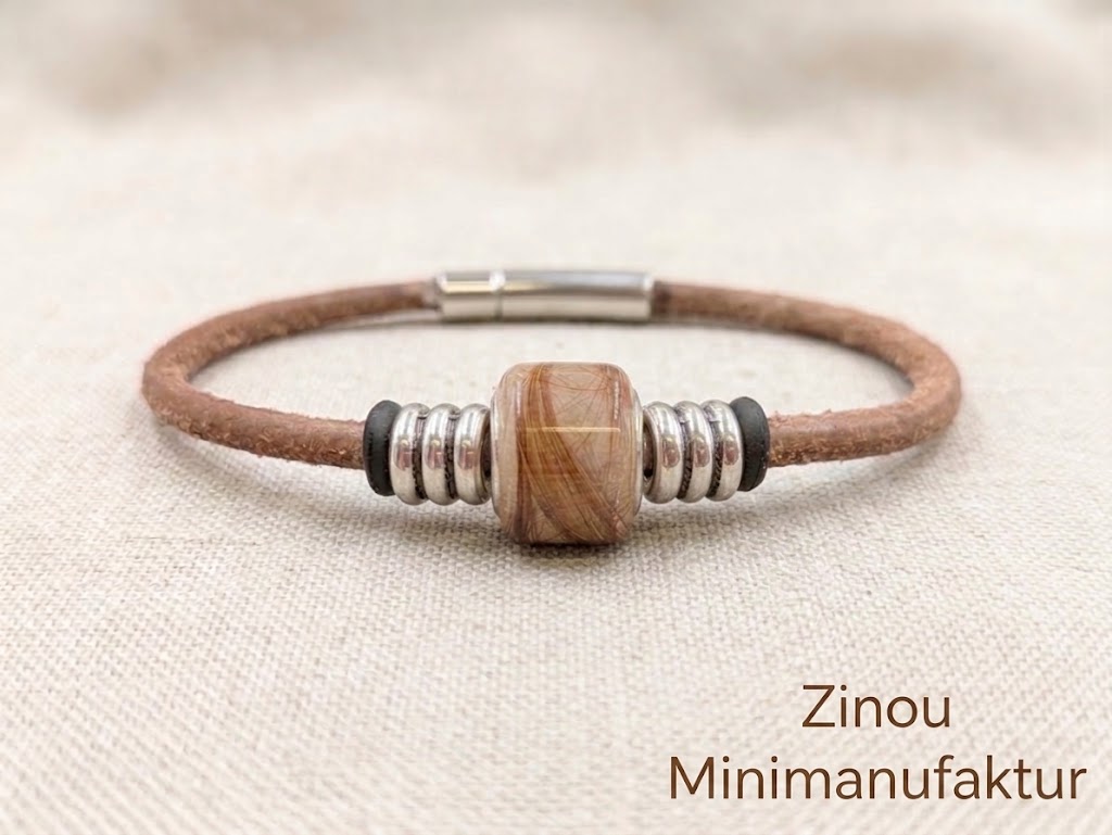 dunkelbraunes Wildlederarmband mit eckiger Perle gefüllt mit Fell vom Hund liegt auf hellem Stoff unten rechts steht Zinou Minimanufaktur