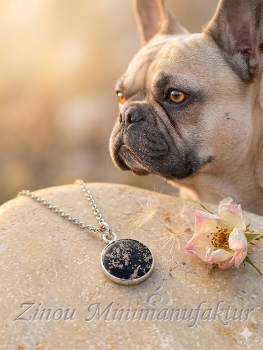 Silberner Dana-Anhänger mit Asche-Einschluss auf schwarzem Untergrund, Französische Dogge im Hintergrund – Gedenkschmuck von Zinou Minimanufaktur
