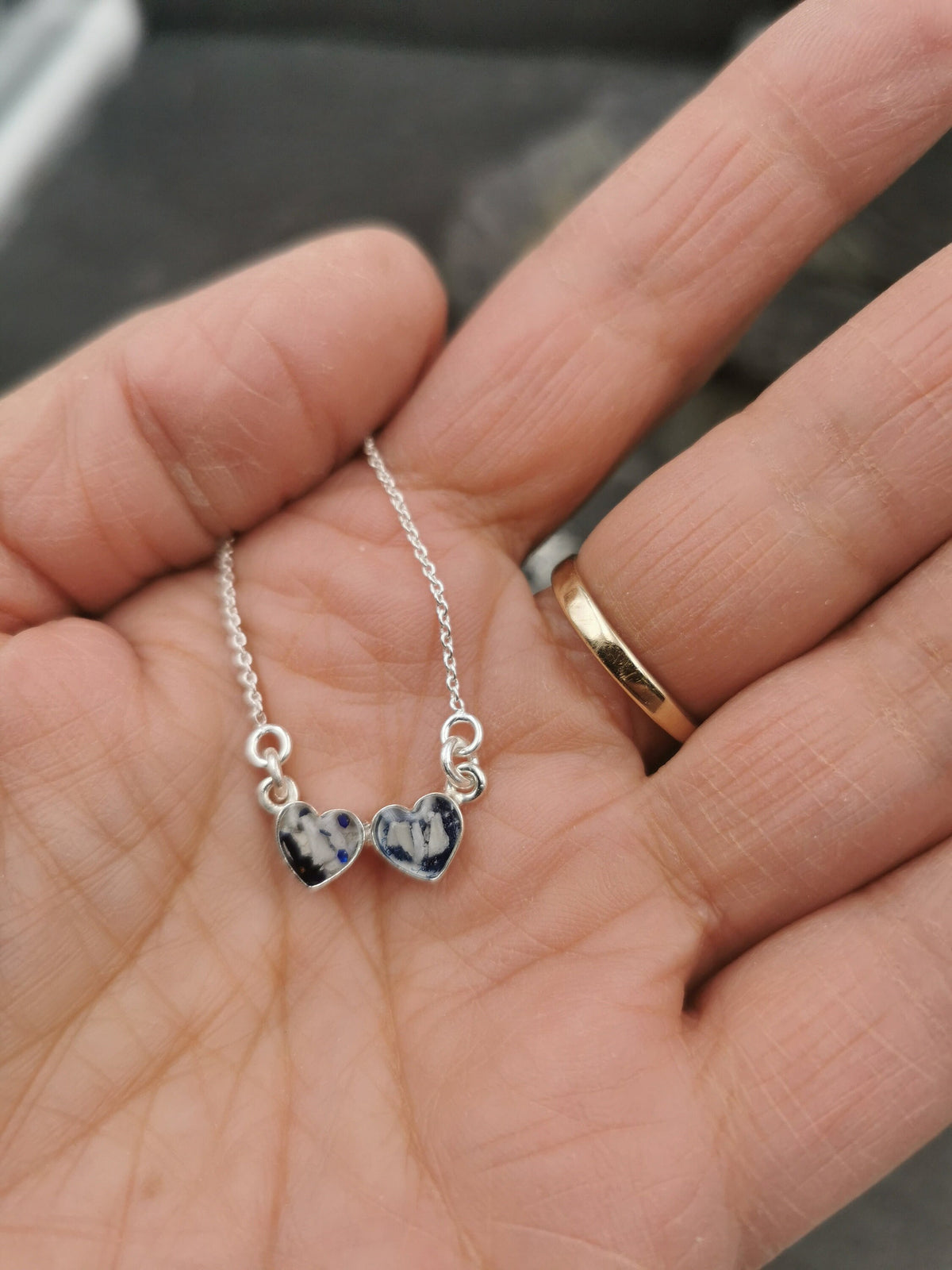 Zwei silberne Herzanhänger mit dunkelgrauem Asche-Einschluss in der Hand gehalten, Nahaufnahme – Gedenkschmuck von Zinou Minimanufaktur