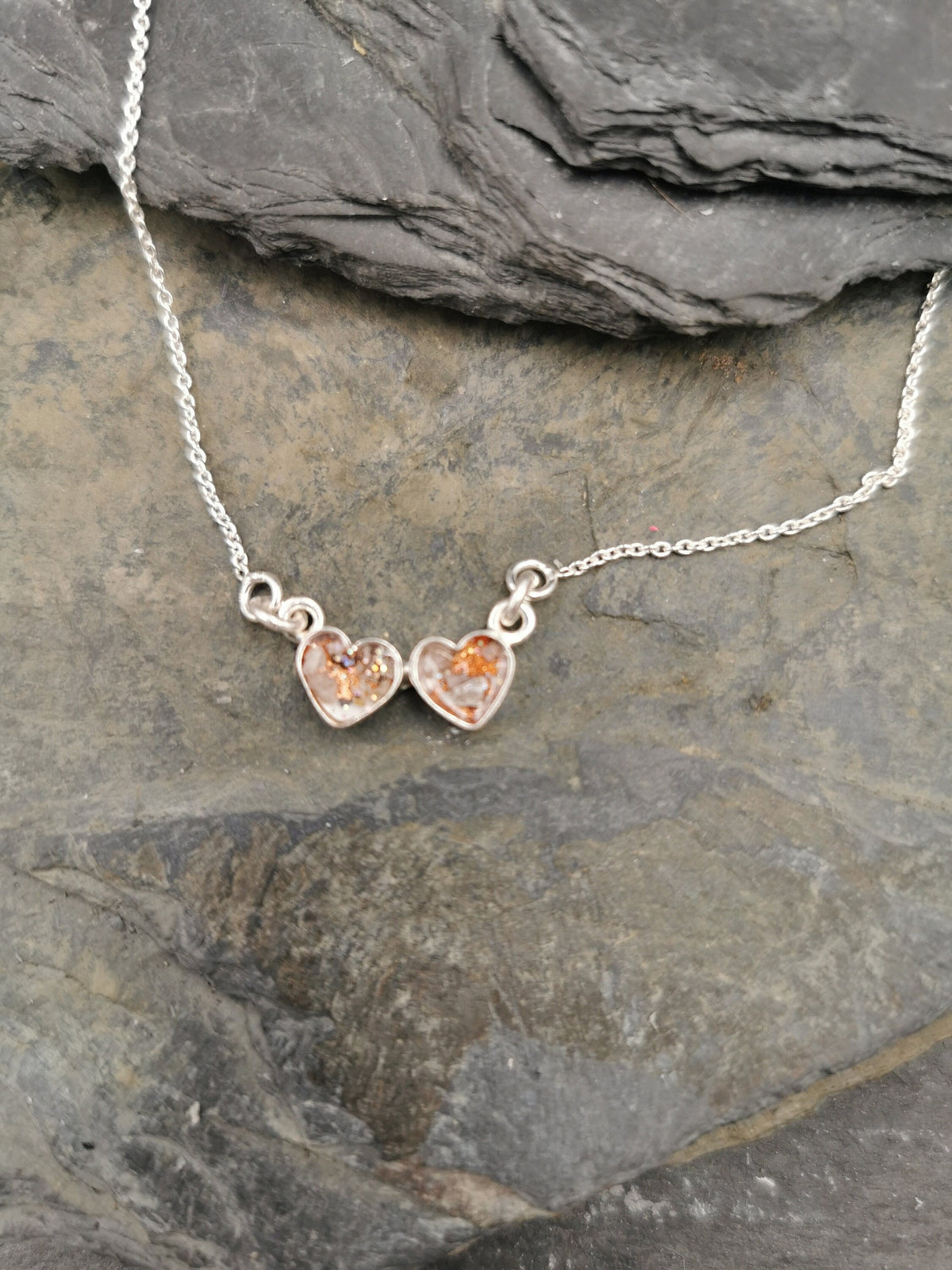 Zwei silberne Herzanhänger mit rosé-goldenem Asche-Einschluss an Silberkette auf Schieferstein – Gedenkschmuck von Zinou Minimanufakt