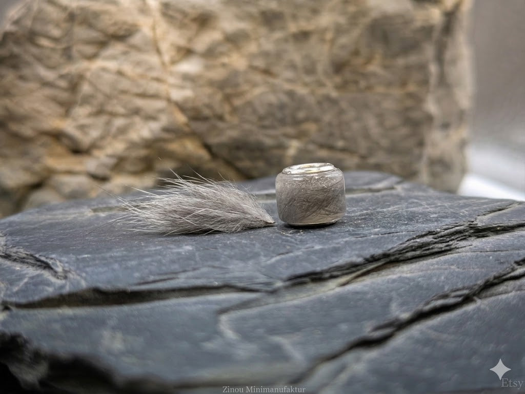 Eckige Großlochperle gefüllt mit hellem Tierhaar auf Schieferstein neben Haarbüschel – Tierhaarschmuck von Zinou Minimanufaktur