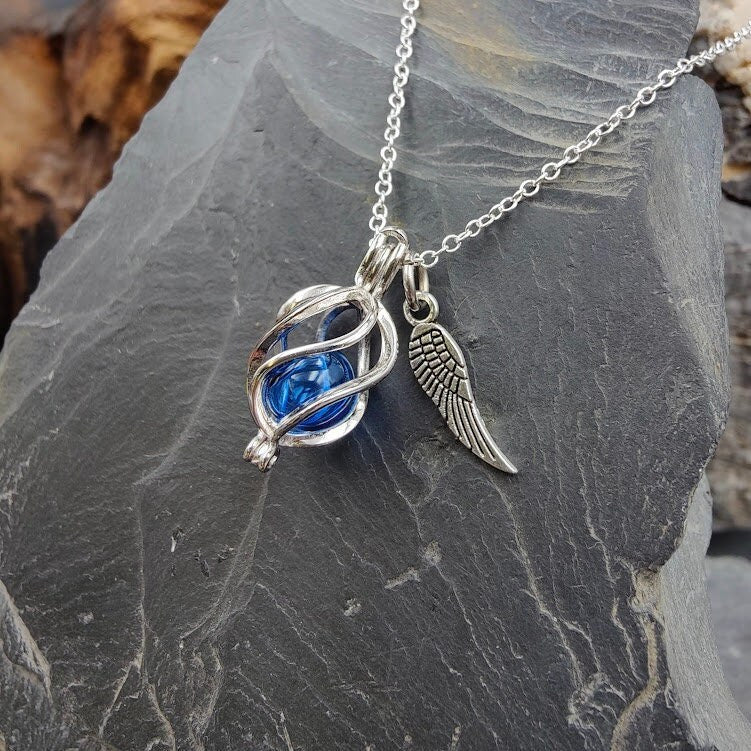 Engelrufer Sterling Silber mit blauer Glasperle und Flügel-Charm an Silberkette auf Schieferstein, Frontansicht – Gedenkschmuck DIY von Zinou Minimanufaktur