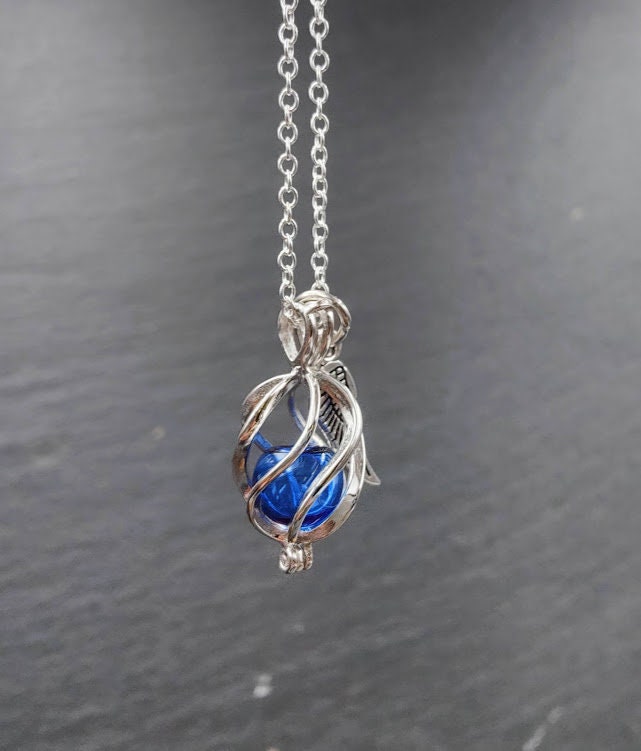 Engelrufer Sterling Silber mit blauer Glasperle hängend an Silberkette vor Schieferhintergrund, Seitenansicht – Gedenkschmuck DIY von Zinou Minimanufaktur