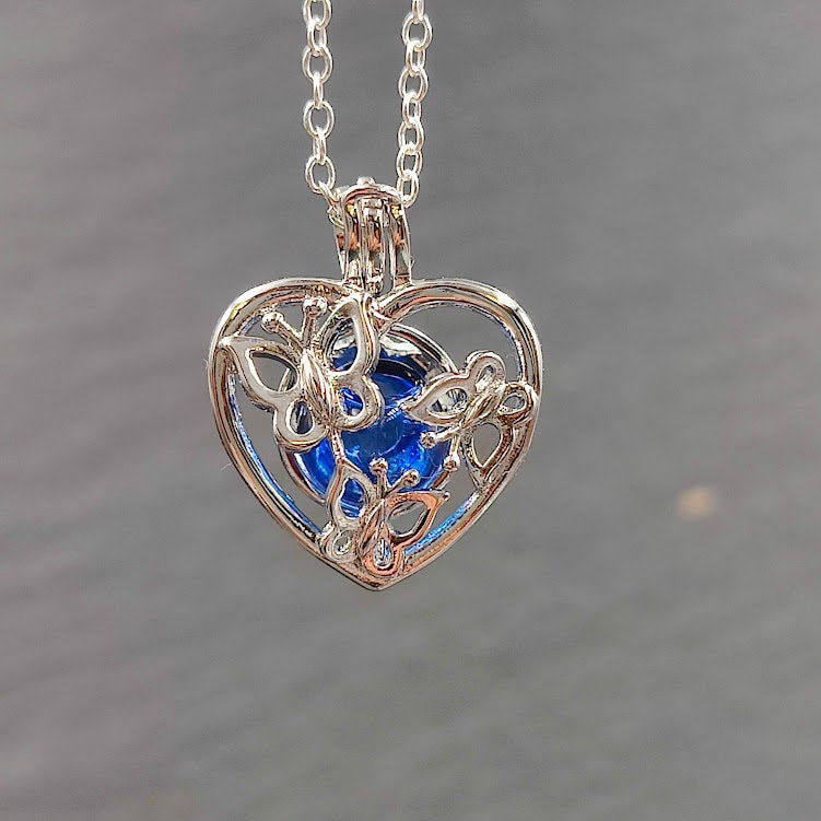 Silberner Herz-Käfig-Anhänger mit Schmetterlingsmotiv und blauer Glasperle hängend an Silberkette, Frontansicht – Gedenkschmuck zum selber Füllen von Zinou Minimanufaktur