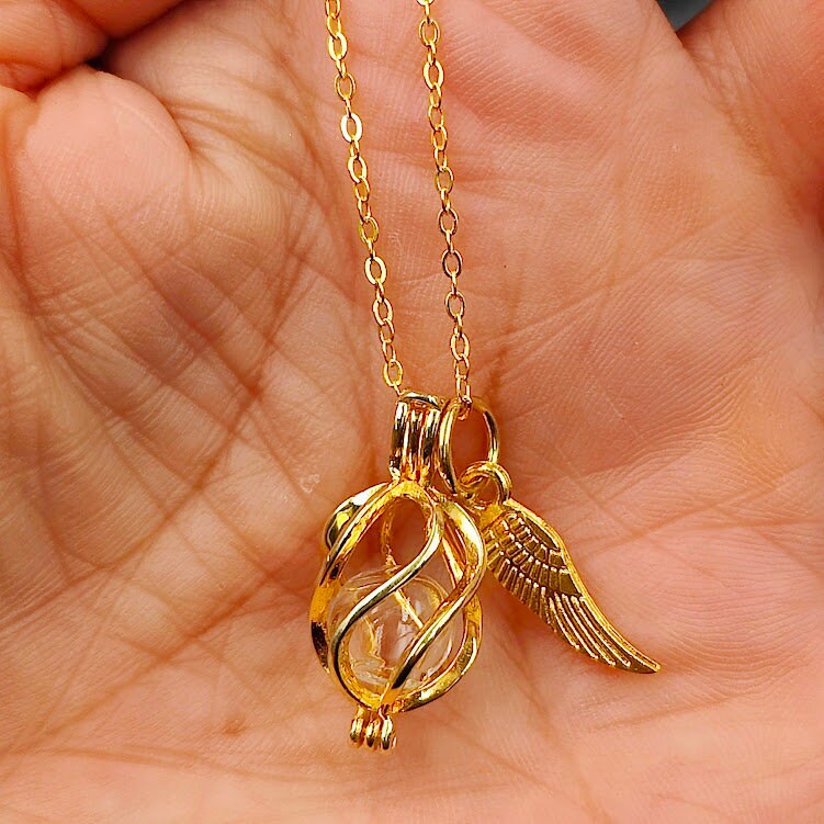 Goldener Käfig-Anhänger mit Flügel-Charm und Glasperle in der Handfläche gehalten – Gedenkschmuck von Zinou Minimanufaktur