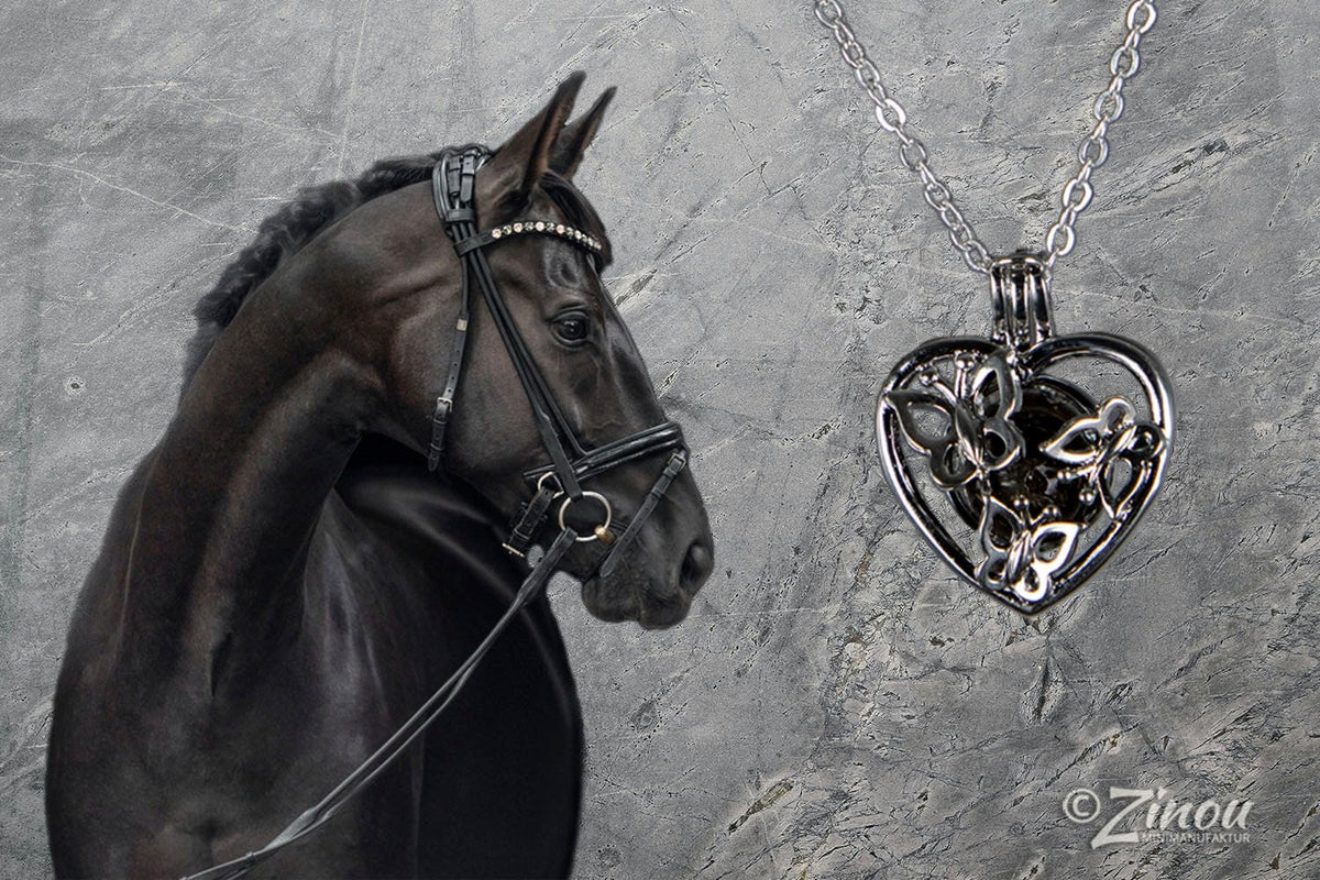 Schwarzer Engelsrufer Herz-Anhänger mit Schmetterlingsmotiv an Silberkette neben schwarzem Pferd-Portrait – Tierhaarschmuck von Zinou Minimanufaktur
