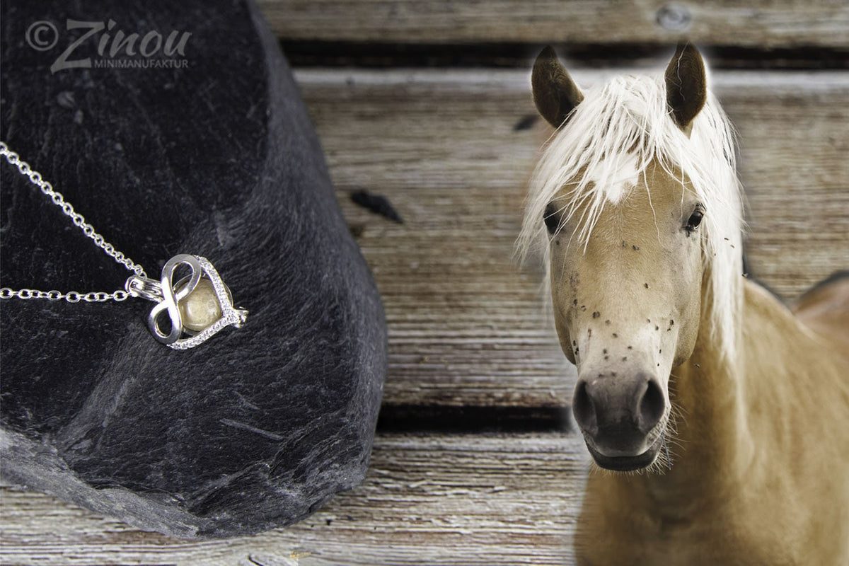 Engelsrufer Infinity-Herzanhänger mit Fell-Perle auf schwarzem Stein, hellbraunes Pferd mit weißer Mähne daneben – Tierhaarschmuck von Zinou Minimanufaktur