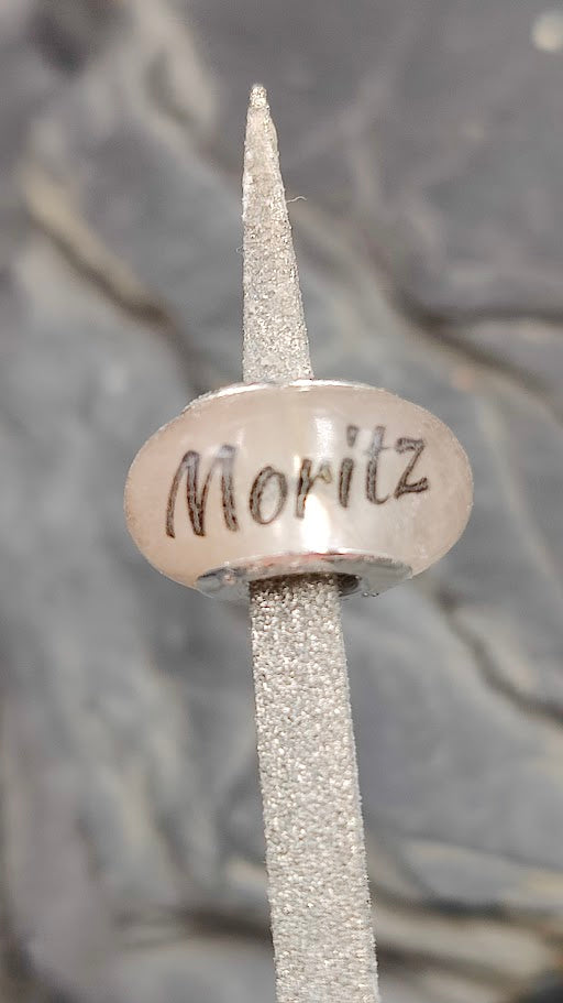 Runde Gedenkperle aus Harz mit dem personalisierten Namen Moritz auf eine Feile gesteckt zur Nahaufnahme der Details