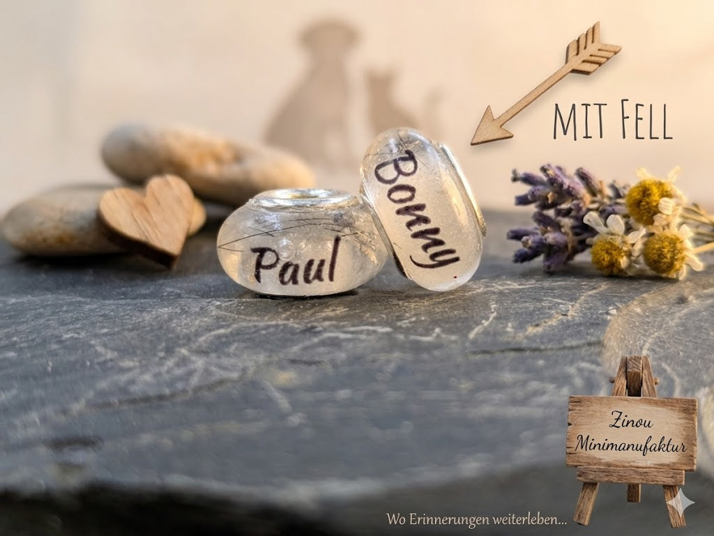 Zwei transparente Gedenkperlen gefüllt mit Tierfell und den Namensaufdrucken Paul und Bonny auf Schieferstein, dekoriert mit Holzpfeil Mit Fell, Trockenblumen und Holzschild Zinou Minimanufaktur