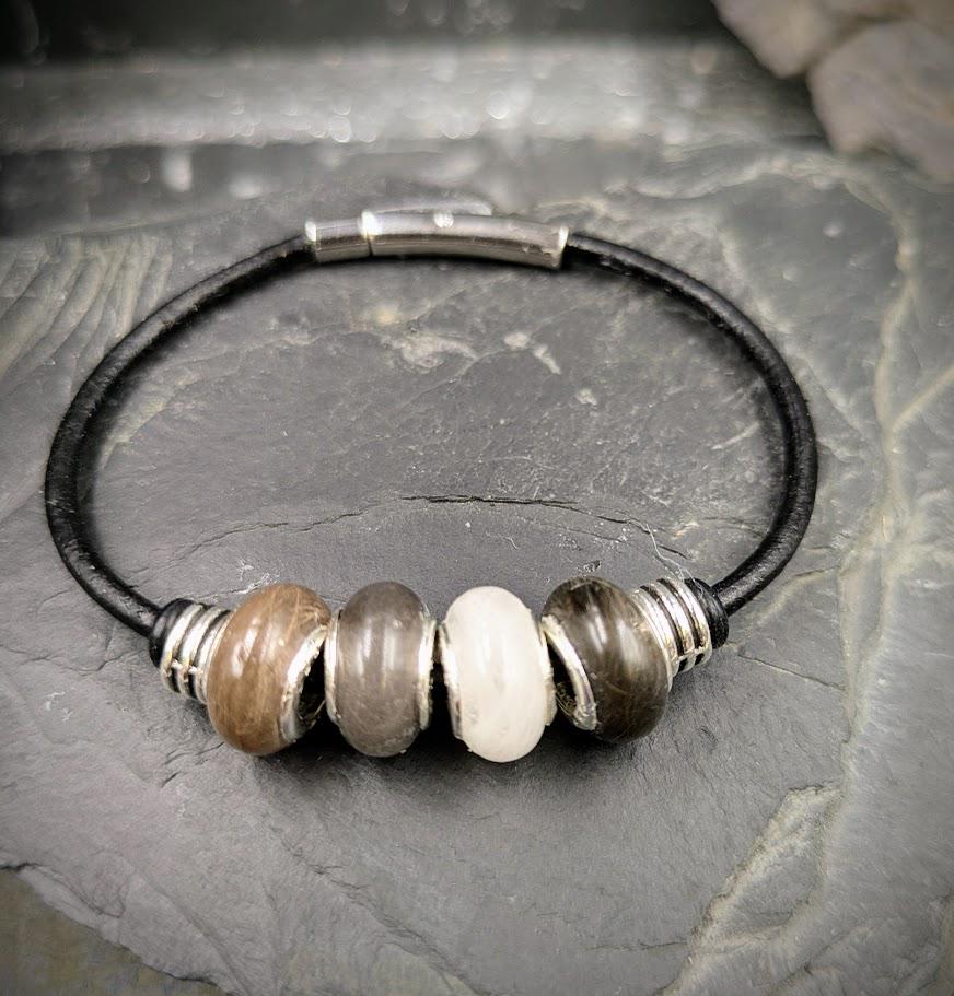 Schwarzes Glattleder-Armband mit drei Minifellperlen in braun-grau und weiß sowie silbernem Magnetverschluss auf Schieferstein – Tierhaarschmuck von Zinou Minimanufaktur