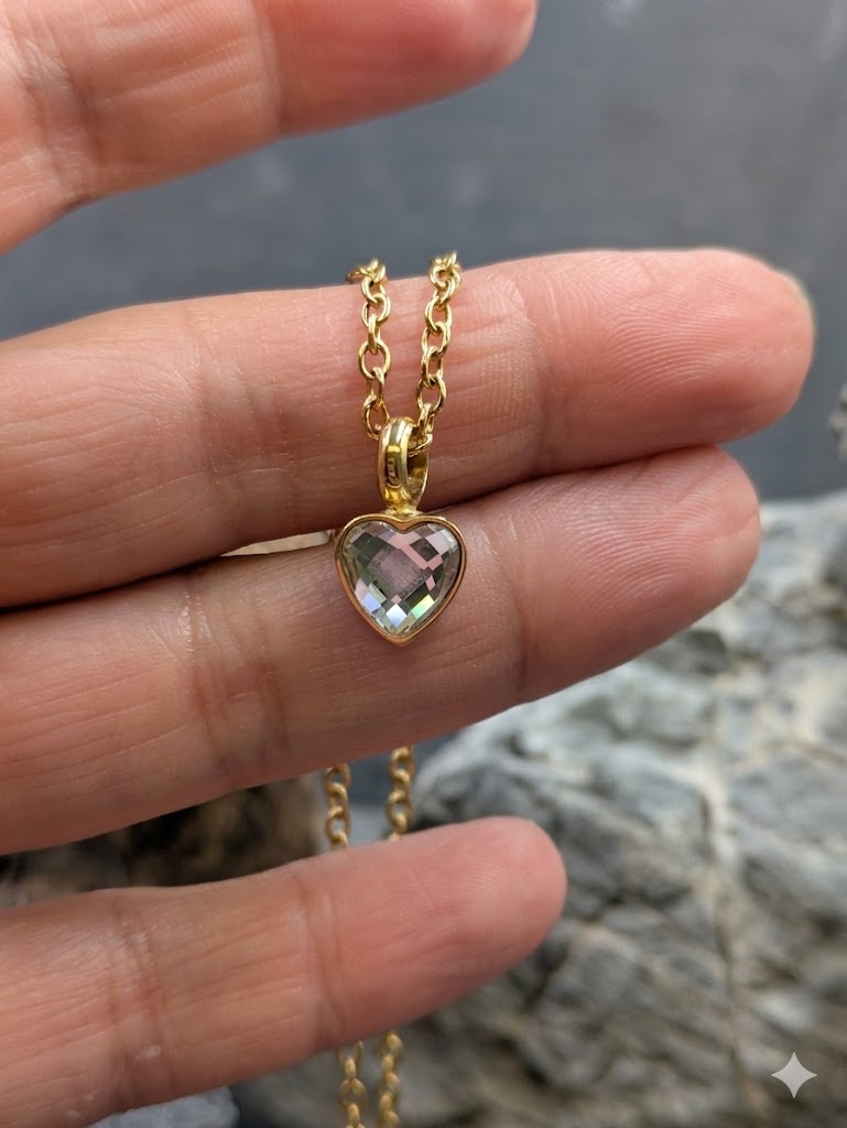 Eine Hand hält eine goldene Halskette mit einem Herzanhänger und gefasstem, transparentem Kristall als befüllbare Mini-Urne