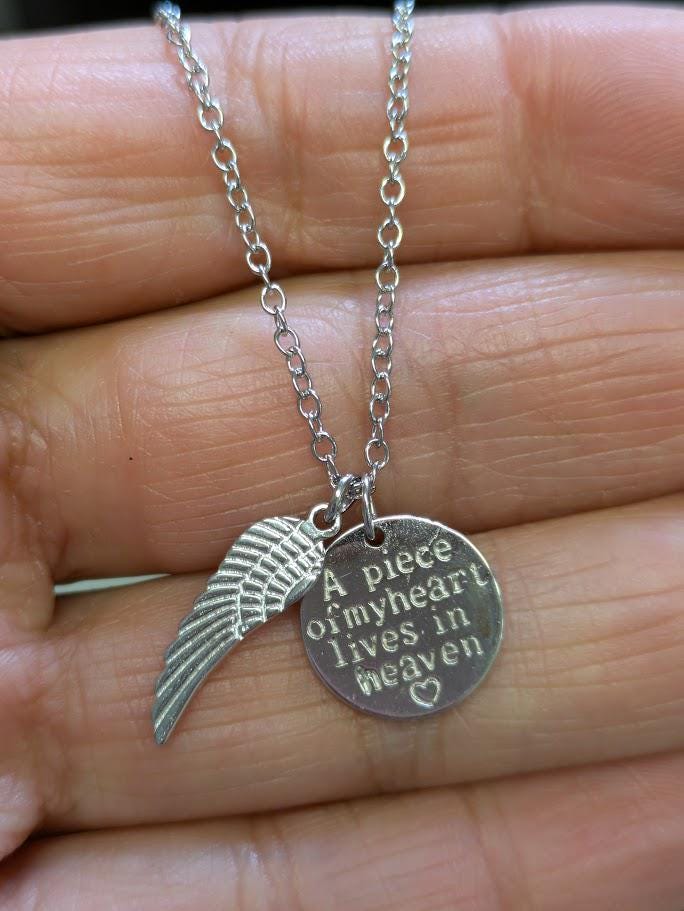 Silberne Heaven-Kette mit Flügel-Charm und graviertem Anhänger „A piece of my heart lives in heaven" in einer Handfläche gehalten, Nahaufnahme – Gedenkschmuck von Zinou Minimanufaktur