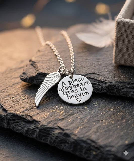 Silberne Heaven-Kette mit Flügel-Charm und rundem Anhänger „A piece of my heart lives in heaven" auf Schieferstein mit Bokeh-Licht – Gedenkschmuck von Zinou Minimanufaktur