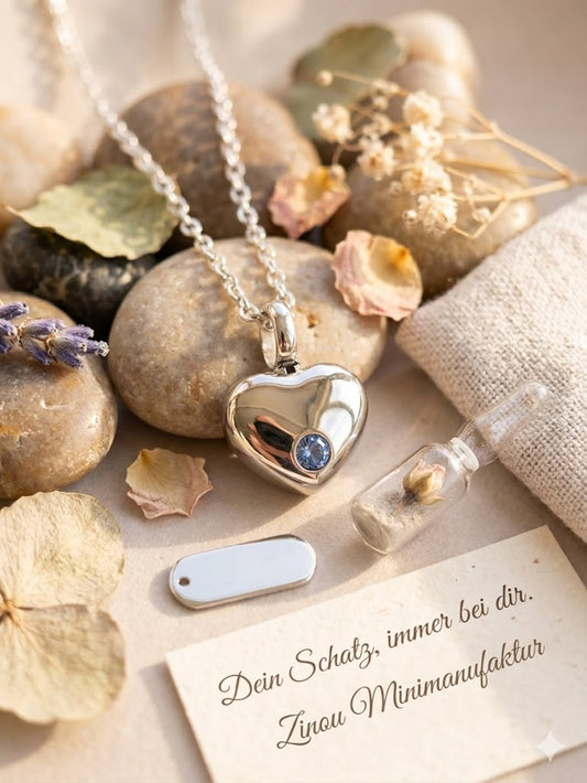 Silberne Herz-Miniurne mit blauem Zirkonia an Edelstahlkette auf Kieselsteinen mit Trockenblumen – Gedenkschmuck von Zinou Minimanufaktur