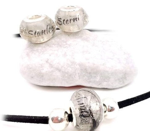 Drei Fellperlen mit gravierten Namen „Stanley\" und „Sterni\" auf weißem Stein, darunter Armband an schwarzer Kordel – Tierhaarschmuck von Zinou Minimanufaktur