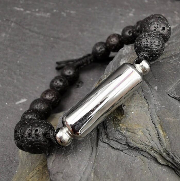 Männerarmband aus schwarzen Lavaperlen mit silberner Miniurne und schwarzem Schnurverschluss auf Fels, Nahaufnahme – Gedenkschmuck von Zinou Minimanufaktur