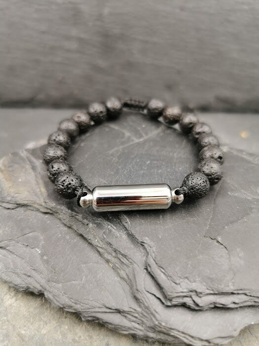 Männerarmband aus schwarzen Lavaperlen mit silberner zylindrischer Miniurne auf hellem Fels, Seitenansicht – Gedenkschmuck von Zinou Minimanufaktur