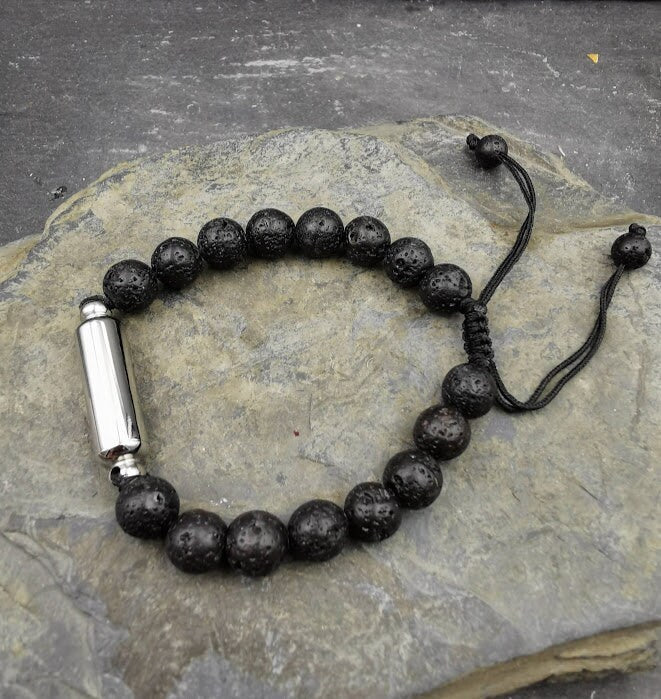 Männerarmband aus schwarzen Lavaperlen mit silberner Miniurne und verstellbarem Schnurverschluss auf Sandstein, Gesamtansicht – Gedenkschmuck von Zinou Minimanufaktur
