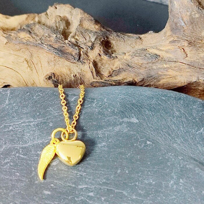 Goldene Miniurne Herz mit Flügel-Charm an Goldkette auf Schieferstein vor Treibholz, Gedenkschmuck von Zinou Minimanufaktur