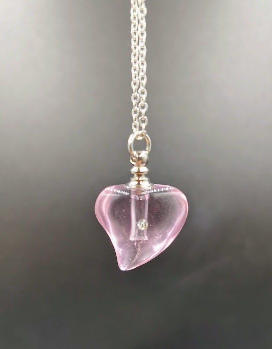 Rosanes Glas-Herz-Urnenanhänger mit Strassstein hängend an Silberkette vor grauem Hintergrund – Miniurne Gedenkschmuck von Zinou Minimanufaktur