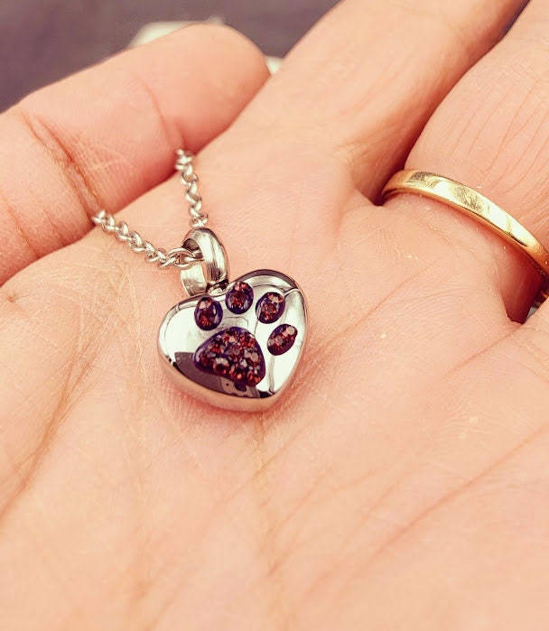 Silberne Herz-Miniurne mit lila Strass-Pfötchen in der Handfläche gehalten, Nahaufnahme – Gedenkschmuck von Zinou Minimanufaktu