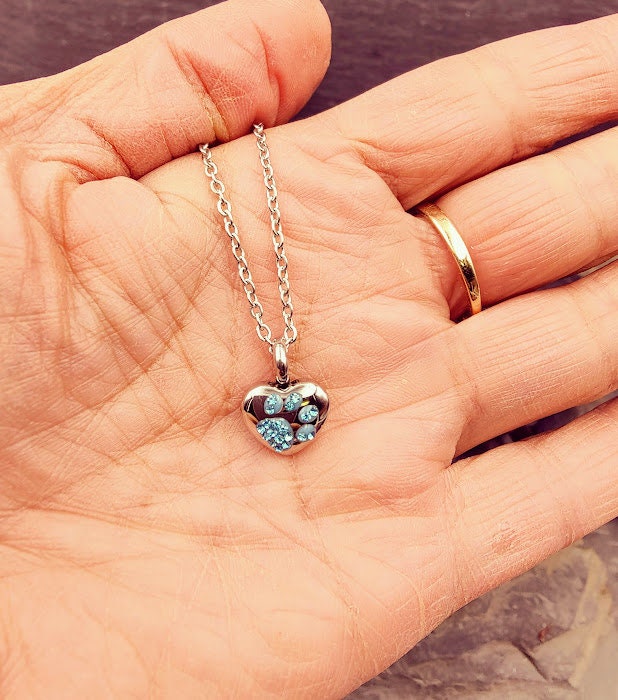 Silberne Herz-Miniurne mit türkisem Strass-Pfötchen in der Handfläche gehalten – Gedenkschmuck von Zinou Minimanufaktur