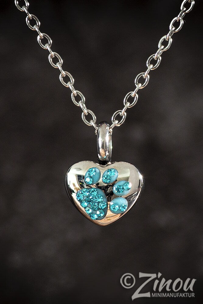 Silberne Herz-Miniurne mit türkisem Strass-Pfötchen hängend an Silberkette, dunkler Hintergrund – Gedenkschmuck von Zinou Minimanufaktur