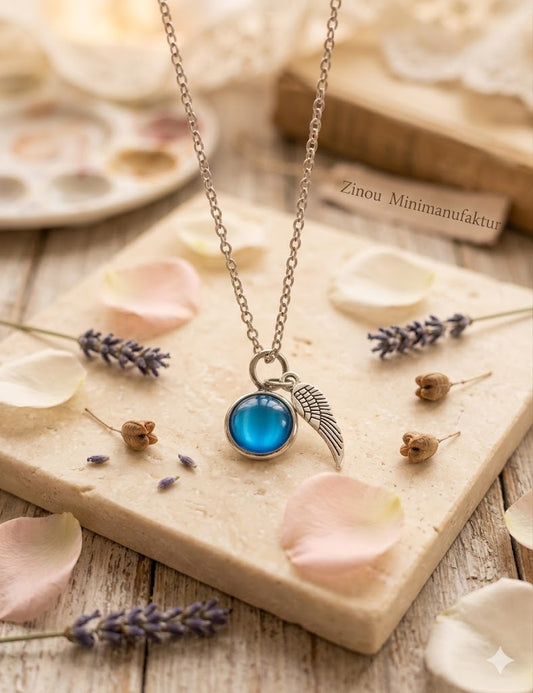 Miniurnen-Anhänger Leni mit türkisblauer Kugel und Flügel-Charm an Silberkette auf Holzplatte mit Rosenblättern – Gedenkschmuck von Zinou Minimanufaktur