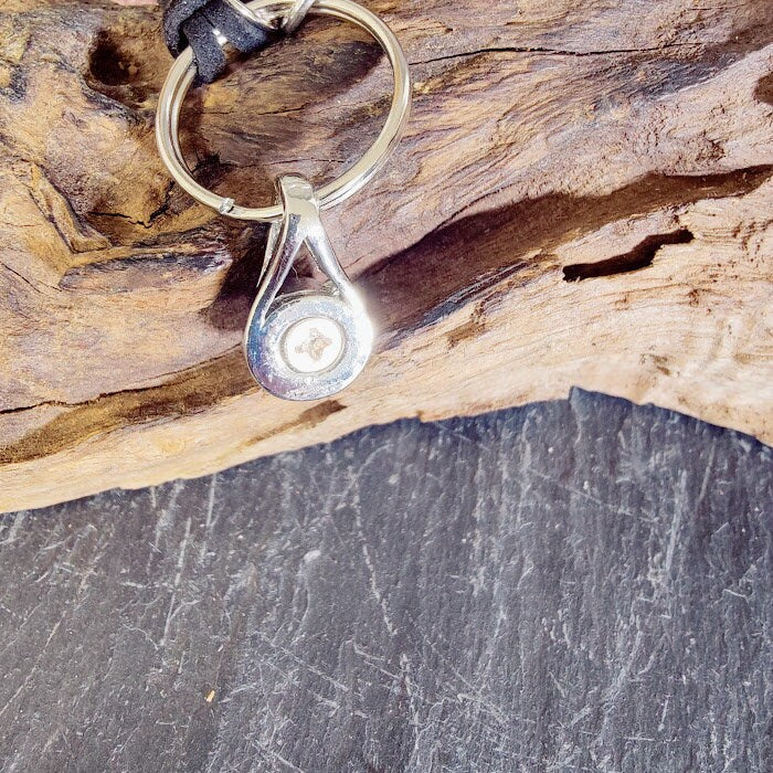 Silberne Tränen-Miniurne am Schlüsselring auf Treibholz, Detailansicht mit sichtbarer Verschlussschraube – Gedenkschmuck von Zinou Minimanufaktur