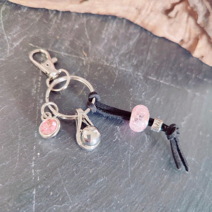 Schlüsselanhänger mit silberner Tränen-Miniurne, rosé Strassstein-Charm und rosa Perle auf schwarzer Lederkordel auf Schieferstein, Draufsicht – Gedenkschmuck von Zinou Minimanufaktur