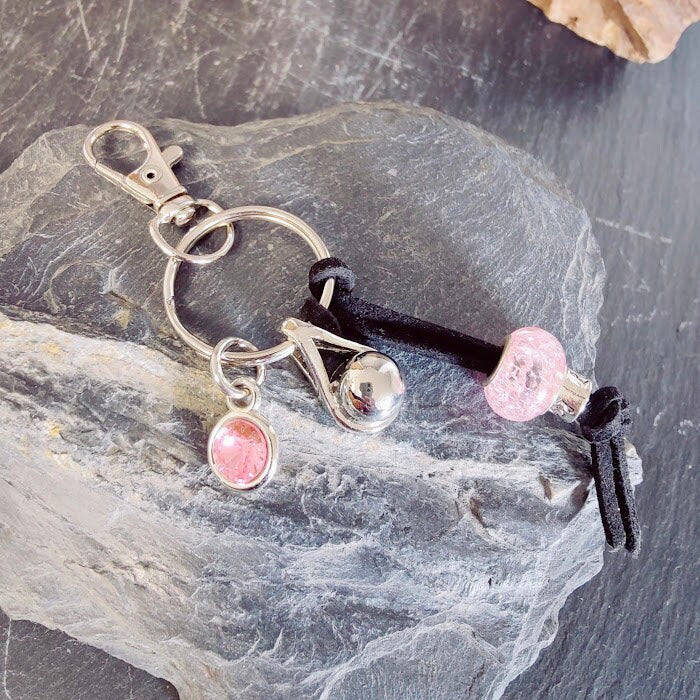 Schlüsselanhänger mit silberner Tränen-Miniurne, rosé Strassstein-Charm und rosa Rosenperle auf schwarzer Lederkordel auf Schieferstein, Frontansicht – Gedenkschmuck von Zinou Minimanufaktur