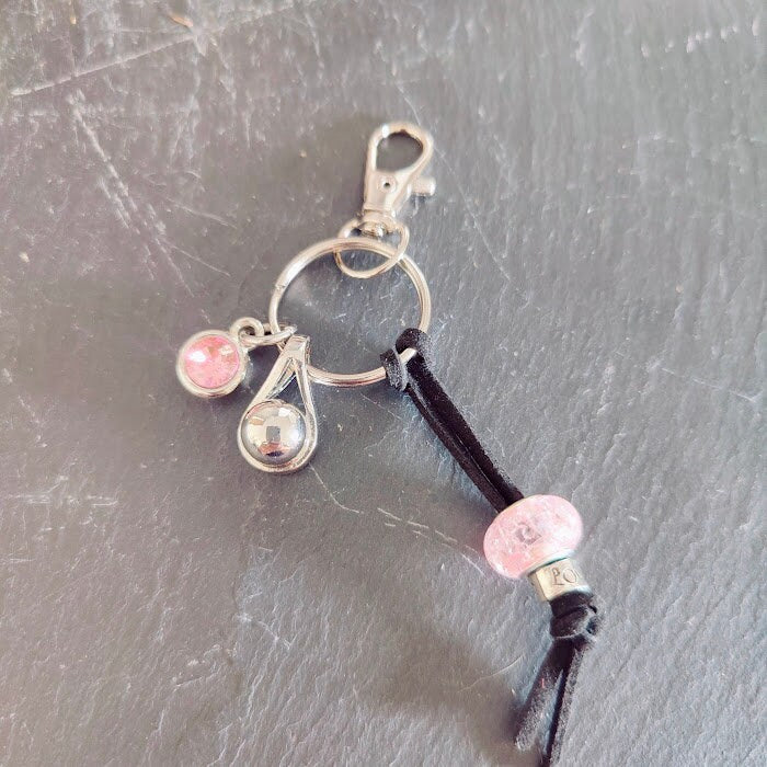 Schlüsselanhänger mit silberner Tränen-Miniurne, rosé Strassstein-Charm und rosa Rosenperle auf schwarzer Lederkordel auf Schieferstein, seitliche Ansicht – Gedenkschmuck von Zinou Minimanufaktur