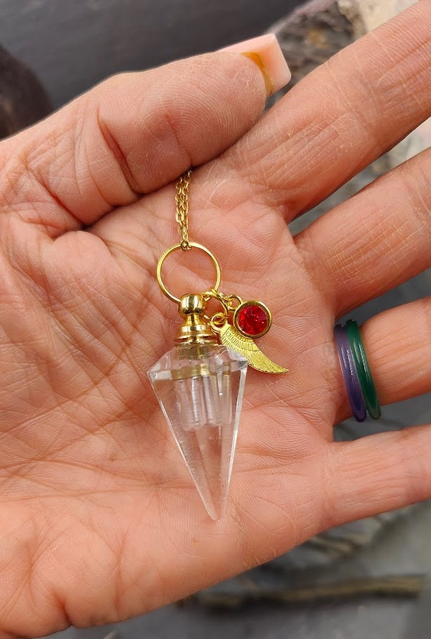 Pendel-Urne aus Bergkristall in der Handfläche gehalten, Flügel-Charm und roter Kristallstein an Goldkette – Gedenkschmuck von Zinou Minimanufaktur