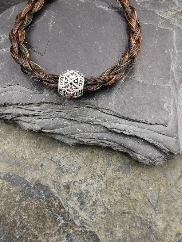 Geflochtenes mittelbraunes Pferdehaararmband mit silberner Perle und rosafarbenen Strasssteinen auf Schieferstein, Nahaufnahme – Pferdehaarschmuck von Zinou Minimanufaktur