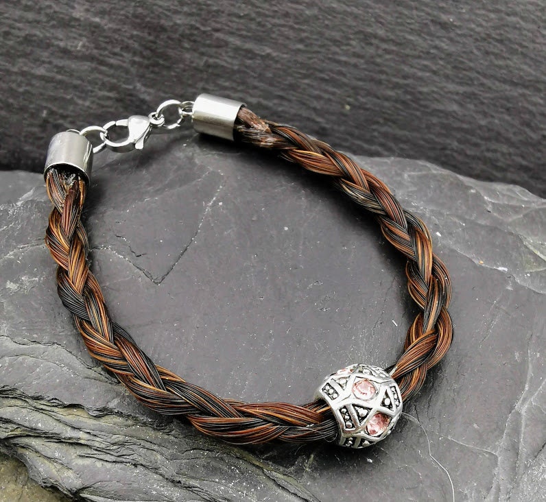 Geflochtenes dunkelbraunes Pferdehaararmband mit ornamentaler silberner Perle und rosafarbenen Strasssteinen auf Schieferstein, Karabinerverschluss sichtbar – Pferdehaarschmuck von Zinou Minimanufaktur
