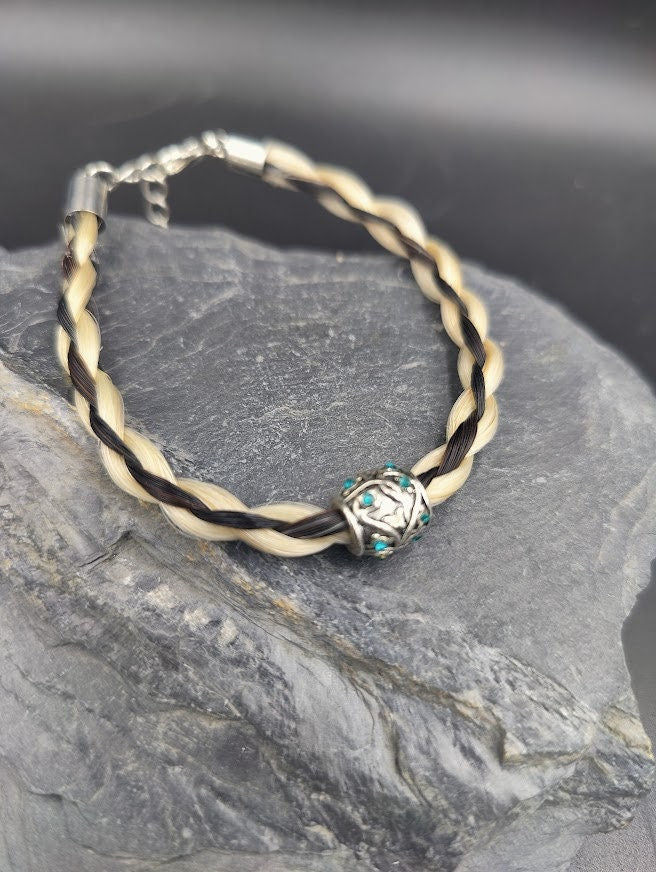 Geflochtenes hell-dunkelbraunes Pferdehaararmband mit silberner ornamentaler Perle und türkisen Steinen auf Schieferstein, Nahaufnahme – Pferdehaarschmuck von Zinou Minimanufaktur