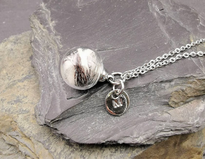 Glasphiole mit Tierhaar und silbernem Buchstaben-Charm M an Silberkette auf Schieferstein, seitliche Ansicht – personalisierter Gedenkschmuck von Zinou Minimanufaktur