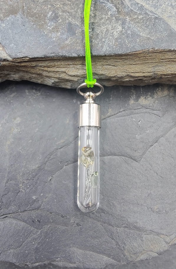 Phiole Röhrchen mit Rosen-Charm hängend an neongrünem Kordel vor Schieferstein – DIY Erinnerungsschmuck von Zinou Minimanufaktur