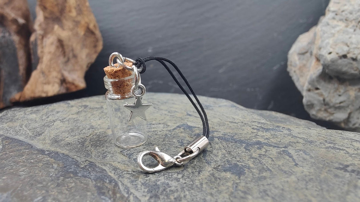 Leere Glasphiole mit Stern-Charm an schwarzer Kordel und Karabiner auf Naturstein – Erinnerungsschmuck DIY von Zinou Minimanufaktur