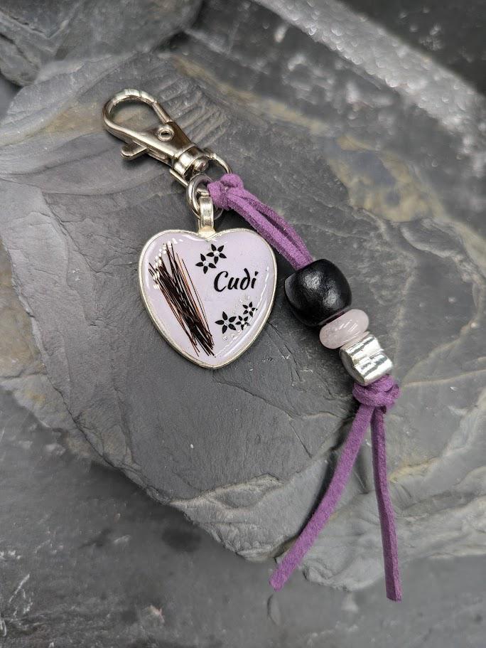 Personalisierter weißlich-lila Herz-Schlüsselanhänger mit schwarzem Tierhaar, Blütenmotiv und Namen Cudi an lila Lederband mit Perlen und Karabiner auf Schieferstein – Gedenkschmuck von Zinou Minimanufaktur