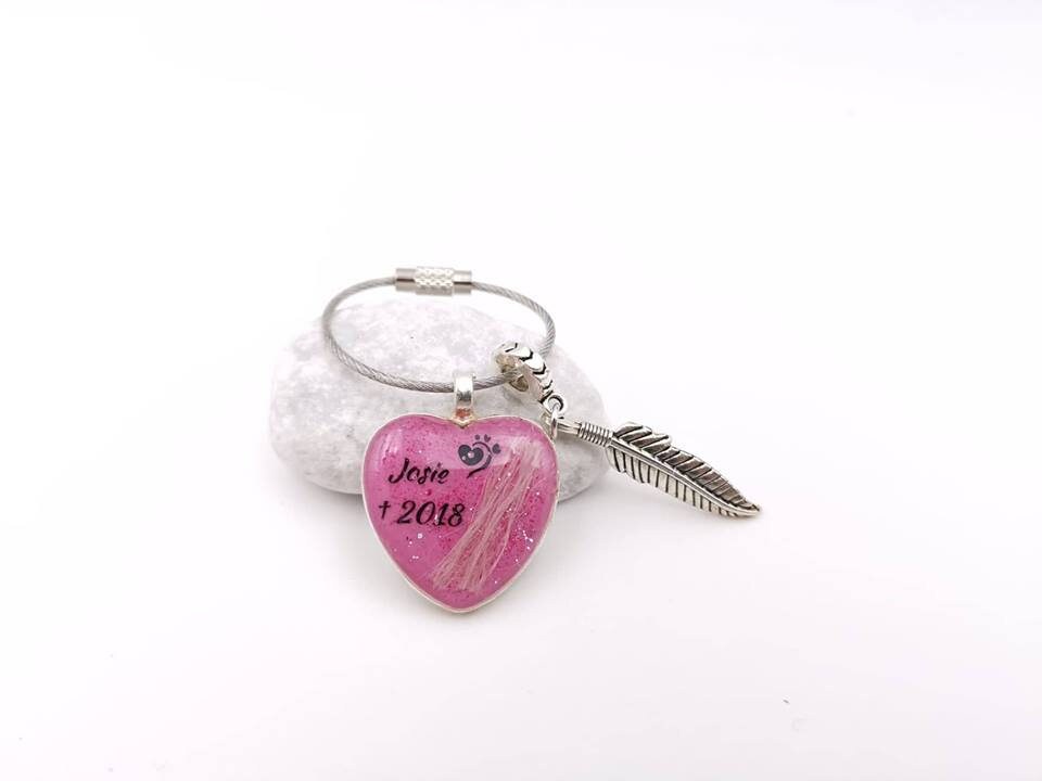 Personalisierter pinker Herz-Schlüsselanhänger mit Tierhaar, Pfoten-Motiv und Aufschrift Josie 2018 an silbernem Drahtring mit Feder-Charm auf weißem Kieselstein – Gedenkschmuck von Zinou Minimanufaktur