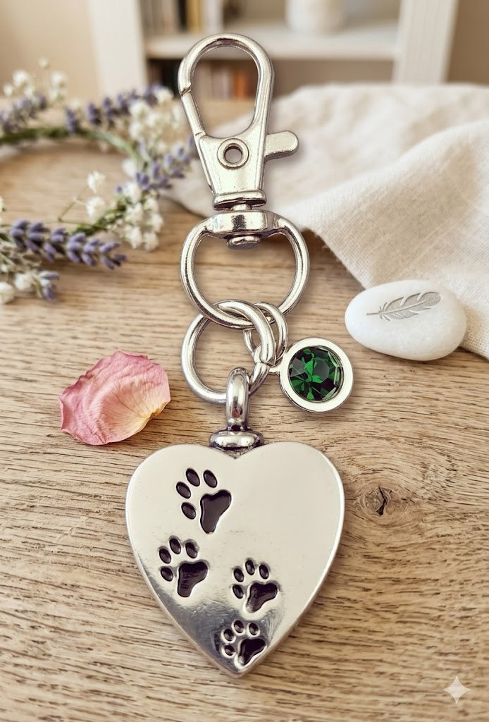 Silberner Herz-Schlüsselanhänger mit Pfotenabdrücken und grünem Strassstein-Charm auf Holztisch mit Lavendel und Rosenblüte – Gedenkschmuck von Zinou Minimanufaktur
