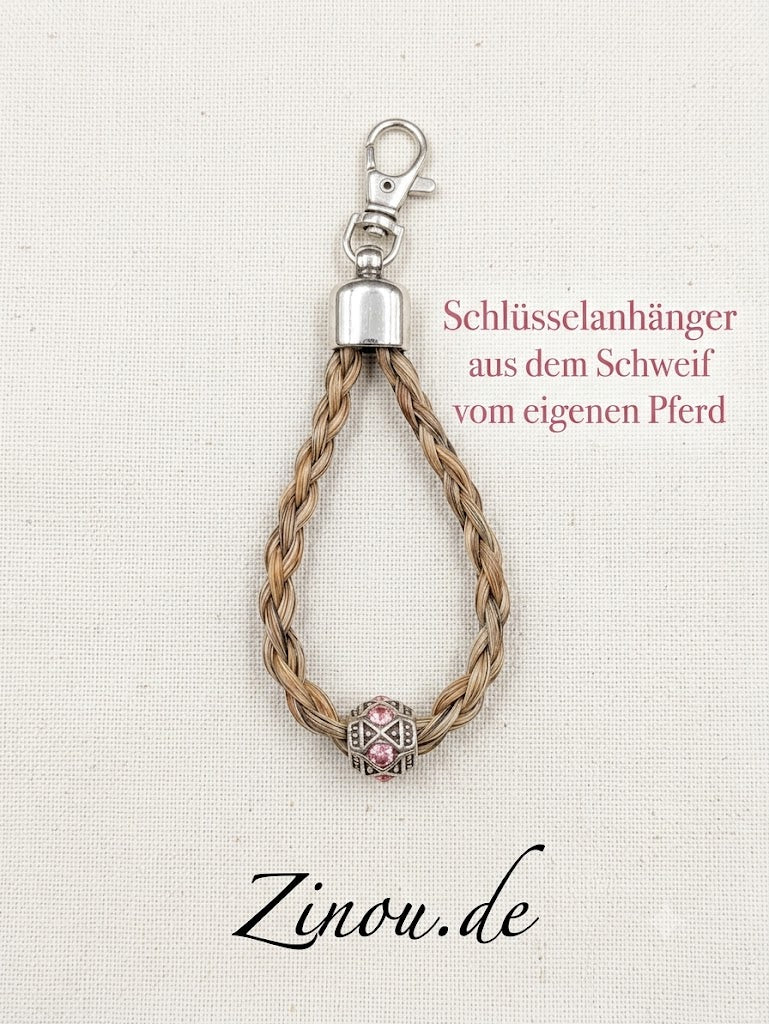 Geflochtener Schlüsselanhänger aus hellem Pferde-Schweifhaar mit Karabinerhaken und rosa verzierter Perle auf hellem Untergrund